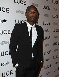 A man in a black suit and white shirt standing before a wall with LUCE, NEON, and topic logos.