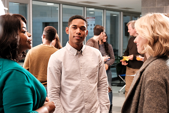 A group of young adults standing and talking in a brightly lit room.