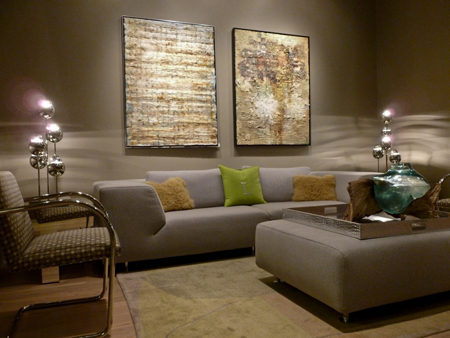 A grey sofa and ottoman in a room with two large abstract paintings and silver orb lamps.