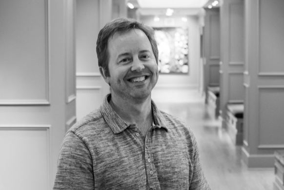 A smiling man with short hair wearing a textured polo shirt, standing in a hallway.