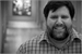Black and white portrait of a man with a beard and a plaid shirt smiling.