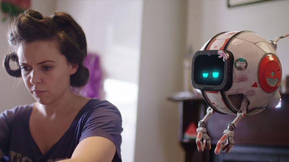 A woman with dark hair looks down while a small, white and red spherical robot floats in the foreground.