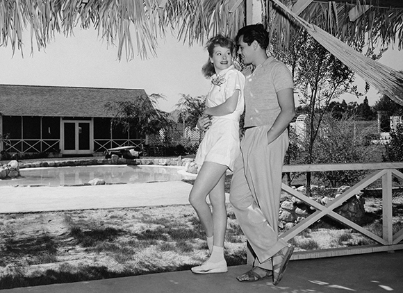 A young man and woman standing together outdoors near a swimming pool.