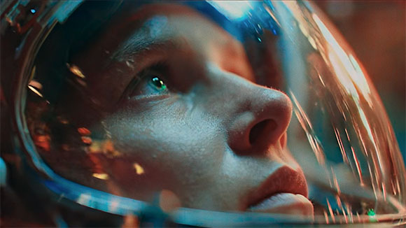 Close-up of a person's face seen through the reflective visor of an astronaut helmet looking upward.