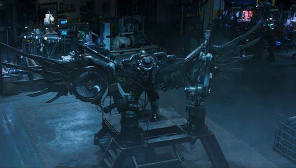 A large, dark mechanical device with metallic wings mounted on a heavy industrial stand in a dim workshop.