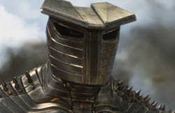 A close-up of a person wearing dark, segmented metallic armor and a heavy helmet.
