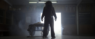 A dark silhouette of a person stands in a doorway filled with bright light and swirling smoke.