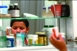 A child's face reflected in a mirror surrounded by various medicine bottles and containers.