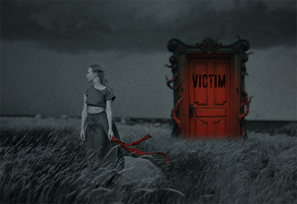 A woman walks through tall grass toward a red door with the word VICTIM on it under a dark, cloudy sky.