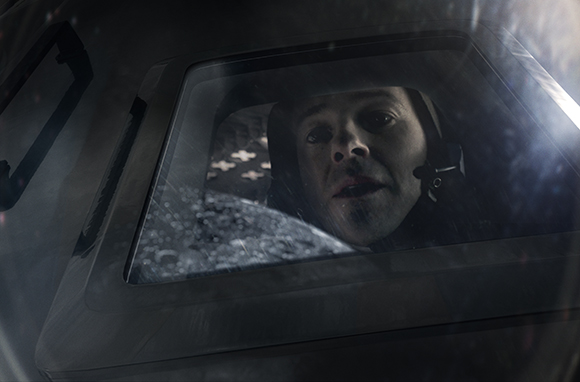 A man with a focused expression looks through a cockpit window during a dark, rainy flight.