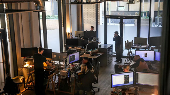 People working at desks with multiple computer monitors in a bright, modern open-plan office.