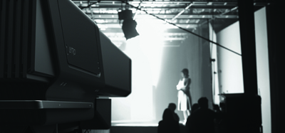 A person stands in a bright spotlight on a dark stage behind large pieces of equipment.
