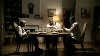 Three men sit around a circular wooden table in a dimly lit dining room.