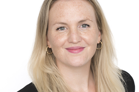 A blonde woman with freckles and gold hoop earrings smiling at the camera.