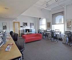 An office with several computer workstations, black chairs, and a bright red sofa in the center.