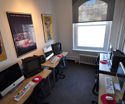 A room with desks, computer monitors, keyboards, and framed posters on the wall.