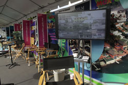 A display booth with chairs and a screen showing a cityscape. Banners and promotional materials are visible.