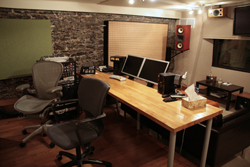 A workspace featuring two long wooden desks, office chairs, computer monitors, and a brick wall.