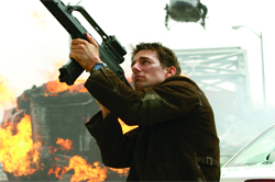 A man in a brown jacket aims a large black weapon toward the sky near a burning vehicle.