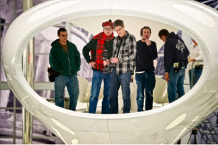 Five men standing together inside a large, white, hollow oval structure.