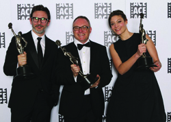 Three people in formal wear holding awards in front of a backdrop with the ACE logo.