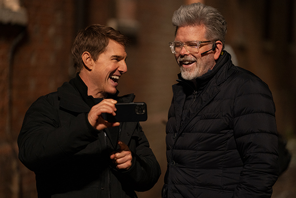 Two men in dark jackets laugh together outdoors during golden hour.
