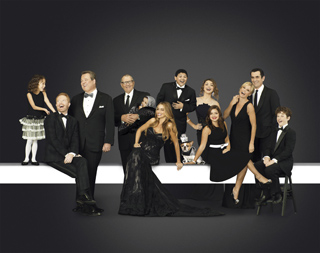 A large group of people in black formal wear posing together against a dark gray background.