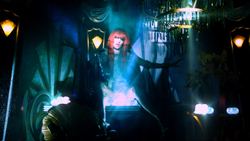 A person with red hair sits in a dark, blue-lit room filled with ornate decor and glowing lights.