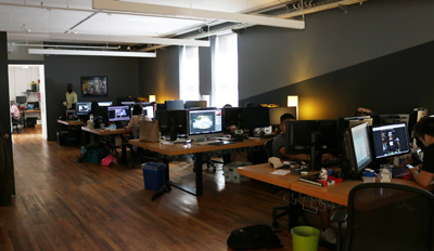 People working at desks with multiple computer monitors in a modern office with wooden floors.