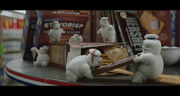 Small white marshmallow figures interact with graham cracker boxes and chocolate bars on a store shelf.