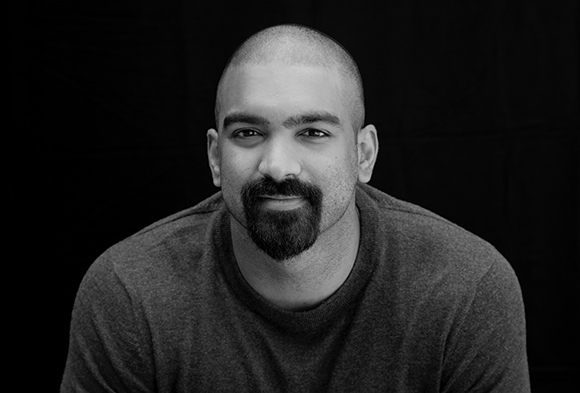 Black and white headshot of a man with a shaved head and a dark goatee looking at the camera.