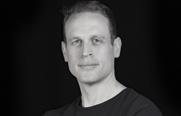 Black and white headshot of a man looking forward against a dark background.