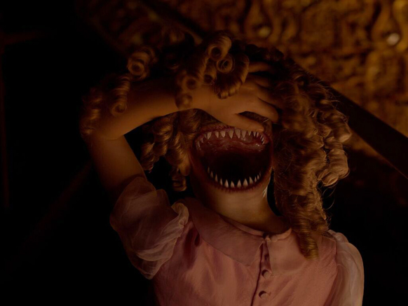 A doll with blonde curls and a wide mouth filled with sharp, jagged teeth.