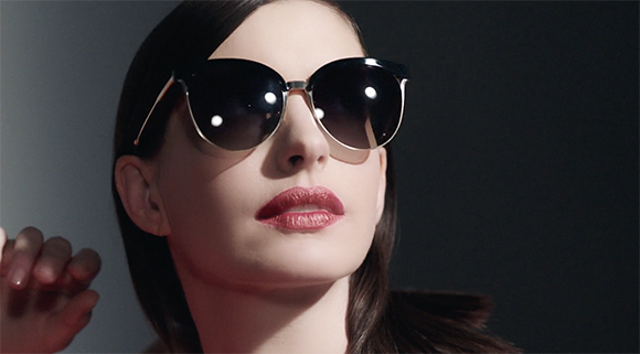 A woman with dark hair wearing large, dark-tinted sunglasses and red lipstick.