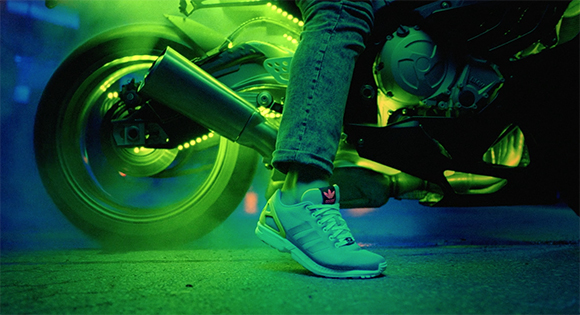 A person in jeans and sneakers sits on a motorcycle glowing with bright green neon light.