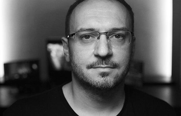 Black and white close-up portrait of a man wearing glasses and looking forward.