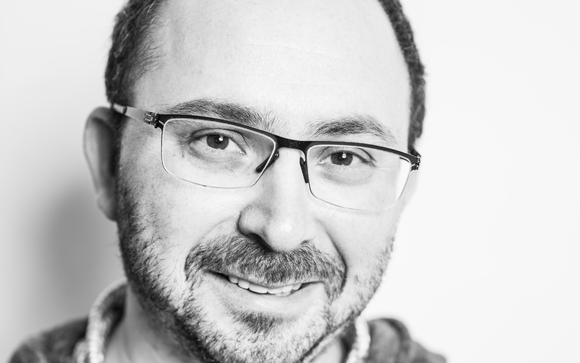 Black and white close-up portrait of a man with glasses and a short beard smiling.