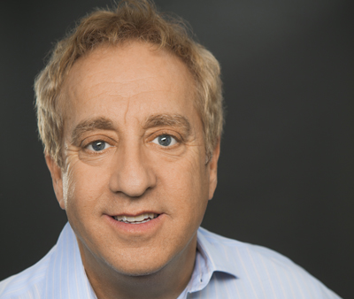 A middle-aged man with blond hair and blue eyes smiling against a dark background.