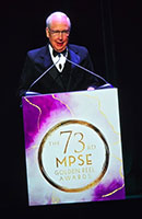 Man in tuxedo speaks at podium with 73rd MPSE Golden Reel Awards logo.