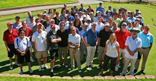 A large group of people standing together on a green lawn outdoors.
