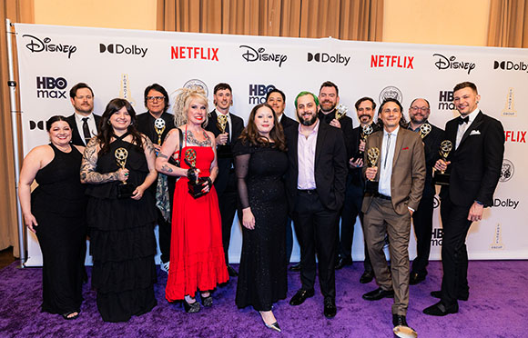 A group of diverse people in formal attire posing together in front of a white backdrop with logos.