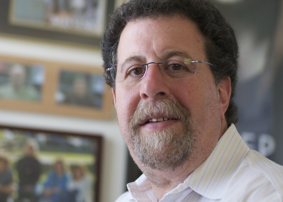 A man with curly dark hair, glasses, and a salt-and-pepper goatee looking toward the camera.