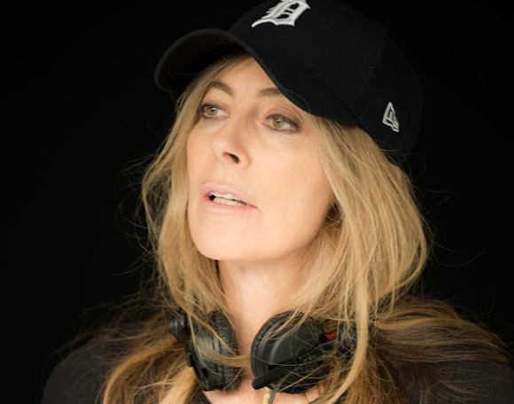 A woman with long blonde hair wearing a black Detroit Tigers cap and headphones around her neck.