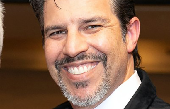 A smiling man with dark hair and a salt-and-pepper goatee looking toward the camera.