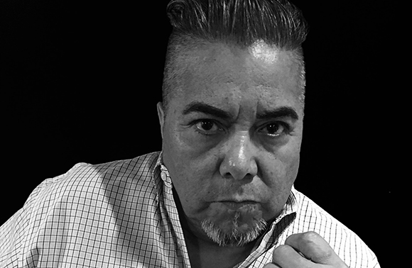 Black and white close-up of a man with a goatee and undercut hairstyle looking forward.