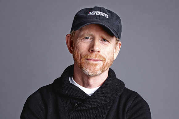 A man with red hair, a beard, and a black cap looking forward against a gray background.