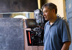 A man in a blue polo shirt stands beside a large professional motion picture camera with a monitor.