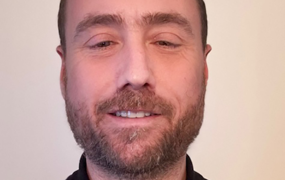 Close-up of a man with short hair and a salt-and-pepper beard smiling slightly.