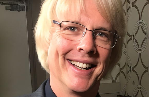 A smiling man with blonde hair and thin-rimmed glasses looking toward the camera.