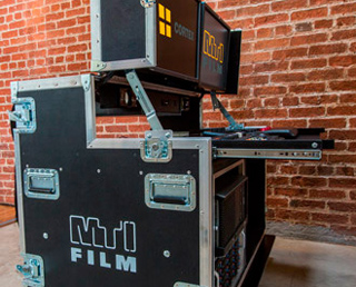 A black professional equipment flight case with an open top compartment and a brick wall background.